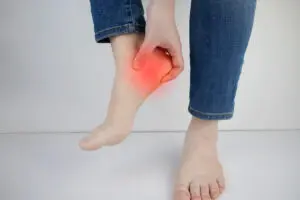 The concept of diseases and pains in the leg. Woman suffering from heel pain. Inflammation or sprain of the tendon in the foot, heel spur, bursitis.